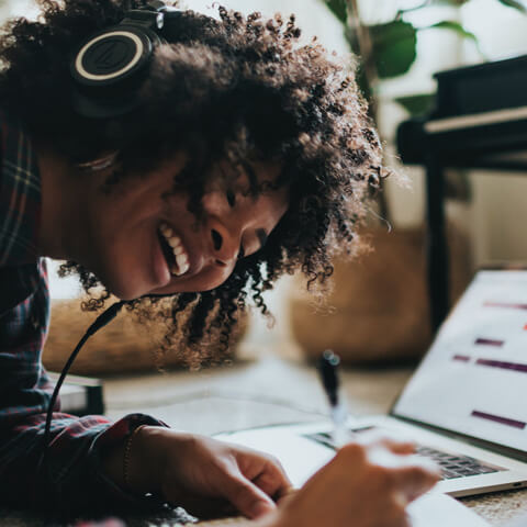 A smiling woman with natural hair listens to headphones. Photo by Soundtrap (Unsplash)