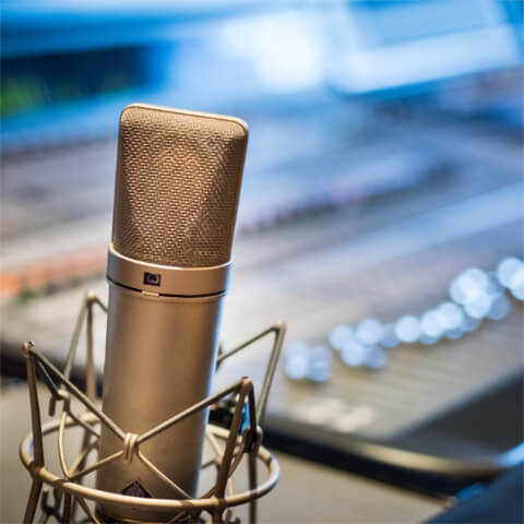 A studio microphone sits in front of a mixing board. Photo by Jacek Dylag (Unsplash)