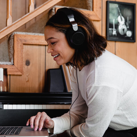 A sitting woman listens to headphones and smiles. Photo by Soundtrap (Unsplash)